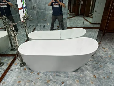 Two freestanding bathtubs with a floor-mount tub filler in a bathroom with mosaic tile flooring.