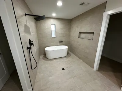 A finished walk-in shower with black fixtures and a freestanding soaking tub in a remodeled bathroom.