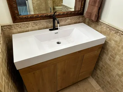 A new bathroom vanity sink with a matte black faucet running water above a wood-tone cabinet.