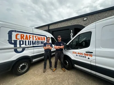 Two Craftsman Plumbing technicians stand between branded service vans outside the shop.
