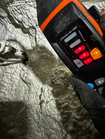 A combustion leak tester with lit indicator lights probes insulation in an attic.