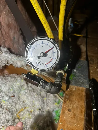 A pressure gauge attached to a flexible gas line during a pressure test in an attic.