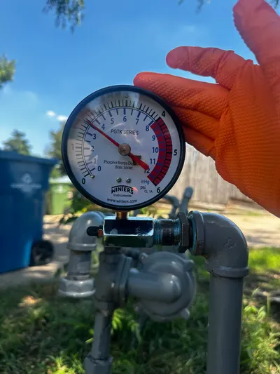 A technician checks a pressure gauge attached to an outdoor gas line for a leak test.