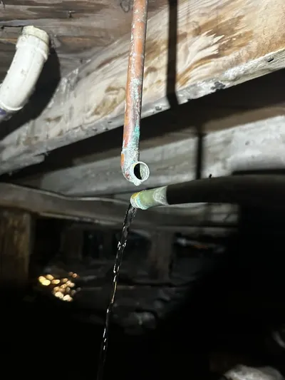 Water sprays from a corroded copper pipe joint beneath a house floor during a leak inspection.
