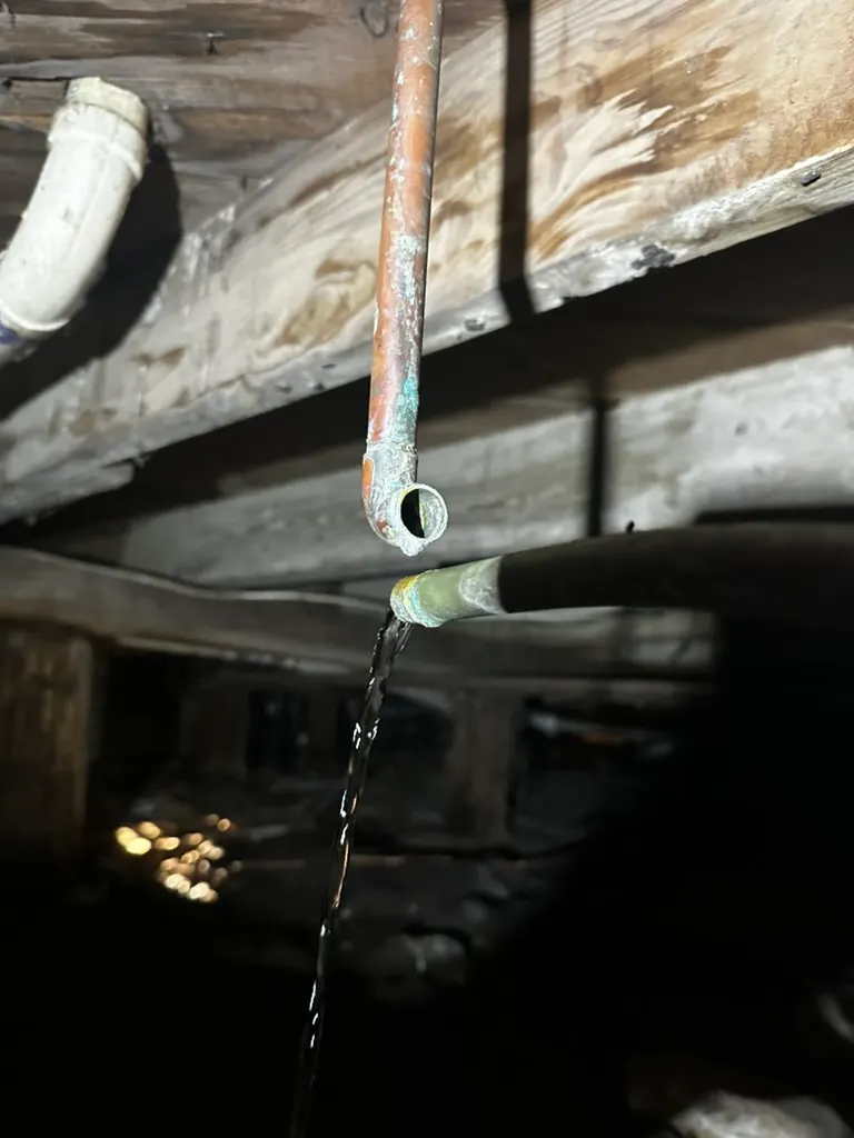 Water sprays from a corroded copper pipe joint beneath a house floor during a leak inspection.