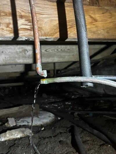Water drips from a copper elbow joint beneath a floor beam before the leak is repaired.