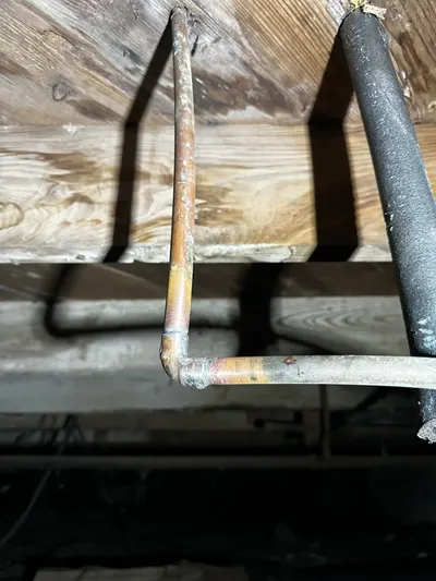 A freshly soldered copper pipe joint repaired beneath a house near a floor beam.