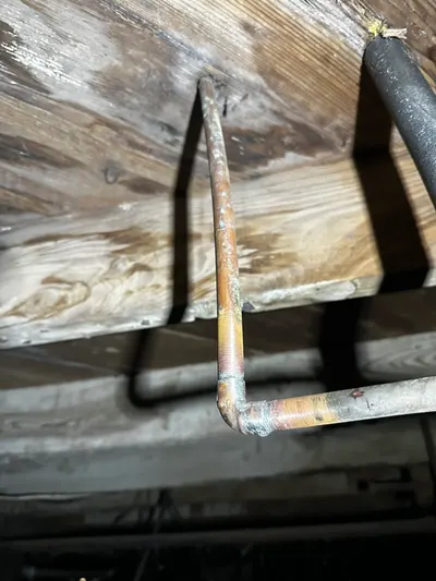 A freshly soldered copper elbow joint repaired in a crawlspace beneath a house.