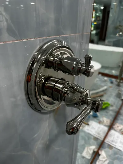 A close-up of a newly installed polished shower valve trim on marble tile above a freestanding tub.