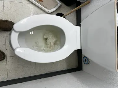 A toilet lifted off its flange during a toilet replacement, with a new unit staged nearby.
