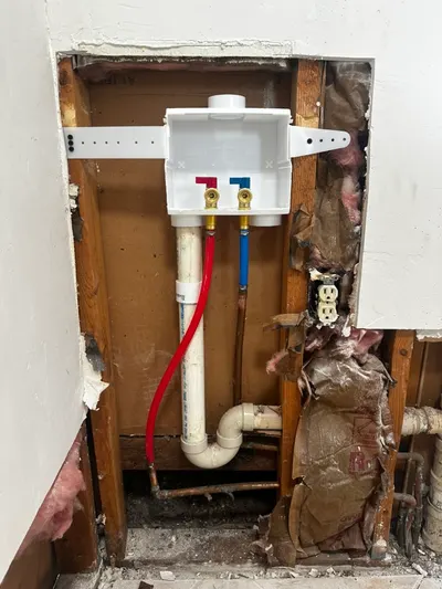 A new washing machine outlet box with hot and cold valves installed in an opened wall cavity.