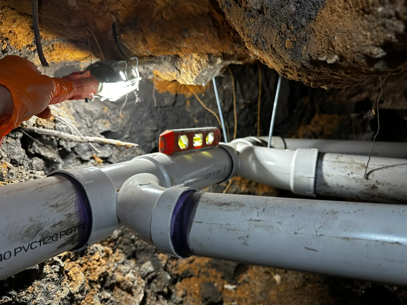 Measuring drainage pipe pitch under slab during sewer line work.