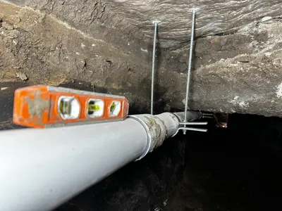 Support sewer pipe by supports hanging from slab during sewer line work.