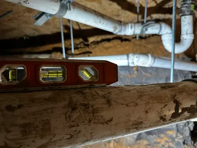 Verifying pitch under slab sewer pipe during sewer line work.