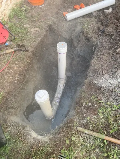 Two capped cleanout pipes standing in a freshly dug yard trench during a sewer line repair.