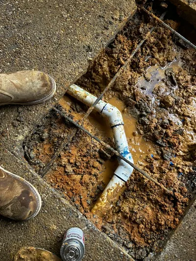 A new PVC pipe fitting installed through a square cut in a concrete slab with rebar exposed.