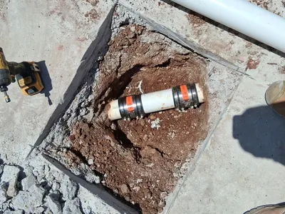 A repaired section of pipe with shielded couplings sits in a square cut through a concrete slab.