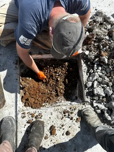 A technician digs through a cut concrete slab to access and repair a leaking pipe.