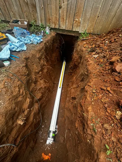 A pipe pushed through a bored trench that runs beneath a wooden fence line.