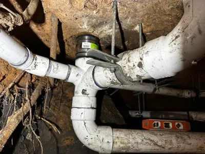 A network of new PVC drain pipes joined and strapped beneath a house in a dug crawlspace tunnel.