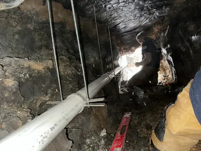A technician works on suspended pipe deep inside a hand-dug tunnel beneath a house.
