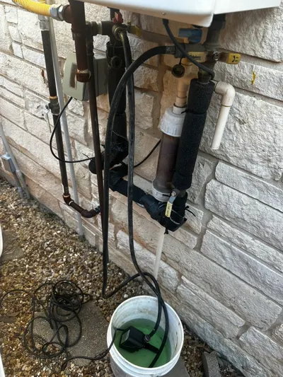Hoses run from an exterior tankless water heater into a bucket during a maintenance flush.