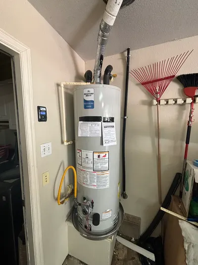A new gas water heater installed in a garage closet next to yard tools.