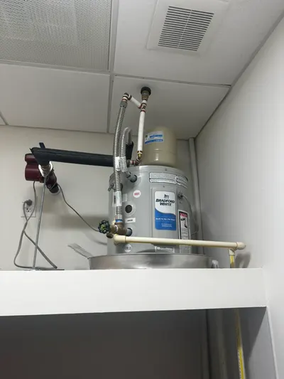 A small electric water heater installed on a shelf in a drop-ceiling utility space.