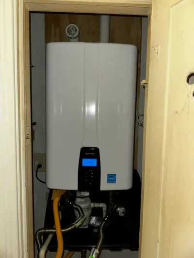 A newly installed tankless water heater mounted in a closet with gas and water lines connected.