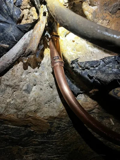 A close-up of a new copper coupling joining a repaired water line in a crawlspace.