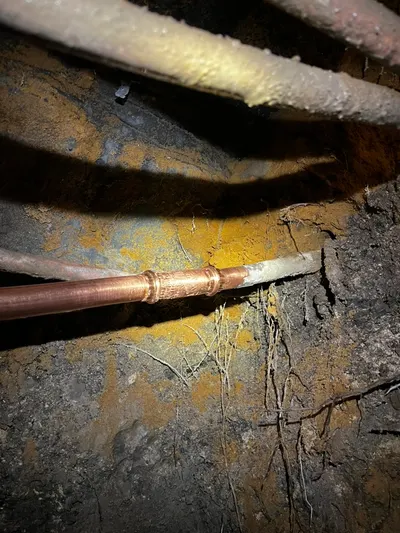 A new section of copper water line joined with a soldered coupling in a dark crawlspace.